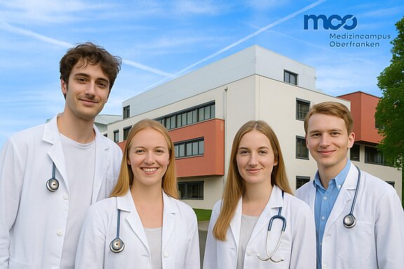 Vier Medizinstudierende in weißen Kitteln stehen lächelnd vor einem modernen Gebäude. Jeder trägt ein Stethoskop um den Hals. Der Himmel ist blau mit wenigen Wolken. Im Hintergrund ist der Schriftzug „Medizincampus Oberfranken“ zu sehen.