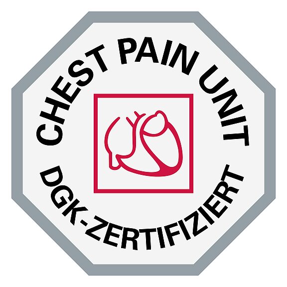 Das Bild zeigt ein sechseckiges Emblem mit der Aufschrift "CHEST PAIN UNIT" und "DGK-ZERTIFIZIERT". In der Mitte befindet sich ein einfaches rotes Symbol eines Herzens. Das Emblem bescheinigt die Zertifizierung eines Brustschmerzzentrums.