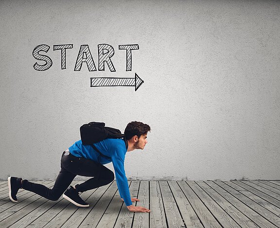 Ein junger Mann in blauer Kleidung steht in der Startposition, bereit zu rennen. Er hat einen schwarzen Rucksack auf dem Rücken und schaut auf den Boden. Über ihm ist das Wort „START“ und ein Pfeil nach rechts an die Wand gezeichnet.