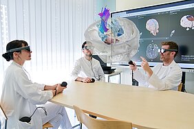 OP-Planung: Eine Ärztin, ein Arzt und Prof. Stefan Linsler aus der Klinik für Neurochirurgie blicken durch VR-Brillen auf das raumfüllende Modell eines menschlichen Gehirns.