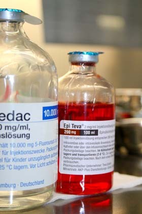 Zwei Glasfläschchen mit medizinischer Lösung stehen nebeneinander. Das linke Fläschchen enthält eine klare Flüssigkeit mit der Bezeichnung "Pedac", das rechte Fläschchen enthält eine rote Flüssigkeit mit der Bezeichnung "Epi Teva". Beide Fläschchen sind für Injektionszwecke vorgesehen.